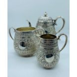 A silver three piece tea set to include teapot, sugar bowl and milk jug with intricate flora design.