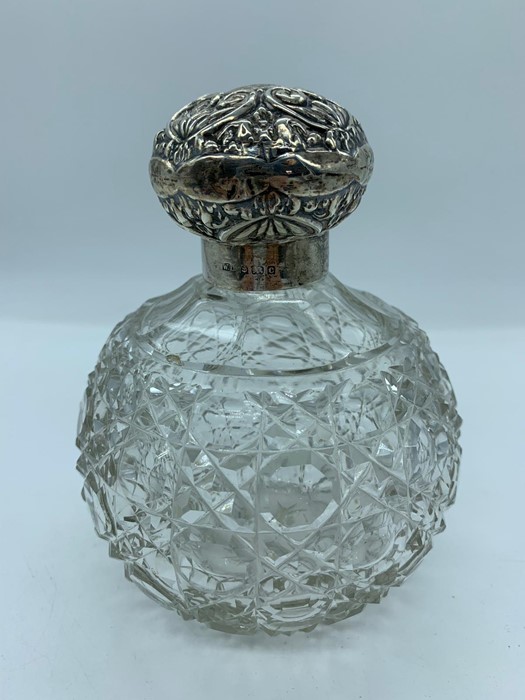 A cut glass scent bottle with hallmarked silver repousse lid