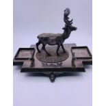 A white metal inkwell stand with stag center and space for inkwells.