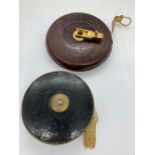 One heavy canvas tape measure in a leather outer case and one in a brass and leather case