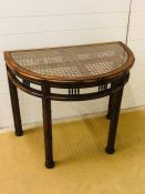 A half moon console table with cane and glass top and bamboo and cane effect frame and legs