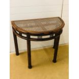 A half moon console table with cane and glass top and bamboo and cane effect frame and legs