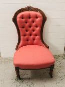 A salmon pink upholstered button back salon chair with carved wooden frame and legs on castors
