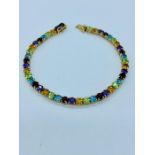 A 9ct gold tennis bracelet with multi coloured stones to include citrine, ruby, aquamarine,