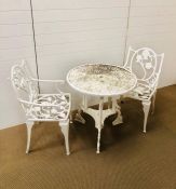 A white painted cast iron garden table with two chairs with arm rests in a floral theme