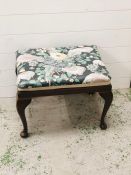 A small upholstered footstool on cabriole legs