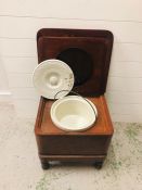 A commode with original pot with lid and handle