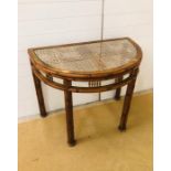 A half moon console table with cane and glass top and bamboo and cane effect frame and legs