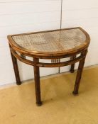 A half moon console table with cane and glass top and bamboo and cane effect frame and legs