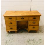 A pine knee hole desk with seven drawers with brass cup handles and small under cupboard on bun