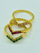 A set of three yellow gold wishbone style rings set with emeralds, rubies and diamonds
