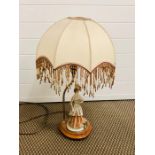 A lamp with a porcelain lady base and beaded fringed shade