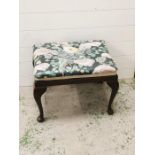 A small upholstered footstool on cabriole legs