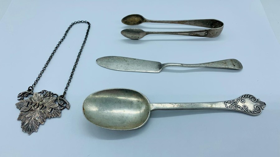 A selection of hallmarked silver items to include: a spoon, butter knife, sugar nips and a Port