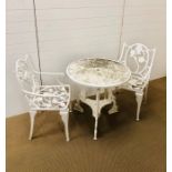 A white painted cast iron garden table with two chairs with arm rests in a floral theme
