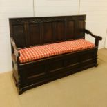 A large carved oak settle in arts and crafts style with hinged seat and base (W184cm H120cm D60cm)