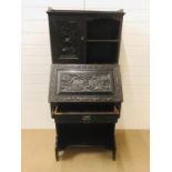 A carved oak writing bureau with cupboard above and drawer under