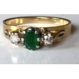 A 18ct yellow gold three-stone emerald and diamond ring: the oval mixed-cut emerald 5.7mm x 4.1mm,