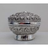 A 19th century Indian silver round box and cover with heavily embossed decoration on a raised