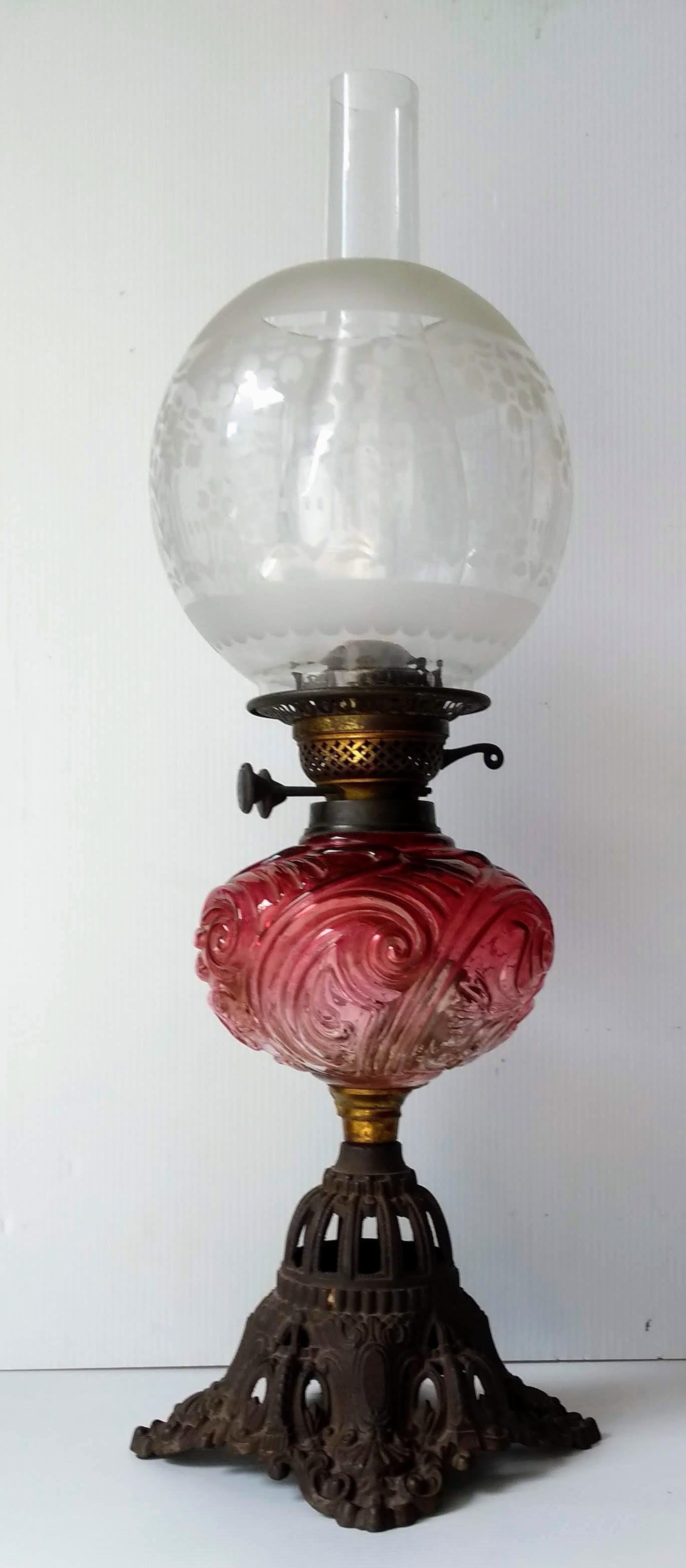 A Victorian ruby glass oil lamp with etched globular shade, chimney, wicks, on a pierced iron base