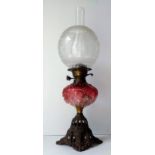 A Victorian ruby glass oil lamp with etched globular shade, chimney, wicks, on a pierced iron base