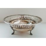 A George V silver concave bowl with pierced decoration on three scrolled feet by James Dixon &