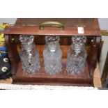 A wooden cased three bottle Tantalus The tantalus with three cut glass diamond pattern decanters,