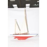 A modern pond yacht With red and white fiberglass hull and wooden deck with two masks and sails,