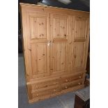 A modern triple pine wardrobe With a moulded cornice above three panelled doors each mounted on full