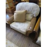 A modern conservatory wicker armchair with loose cushions