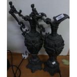 A pair of cast metal decorative ewers, set on plinth bases