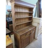 A pine kitchen dresser with three shelves to the back over a base with two doors and drawers