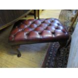 An ox blood red leather footstool on cabriole legs