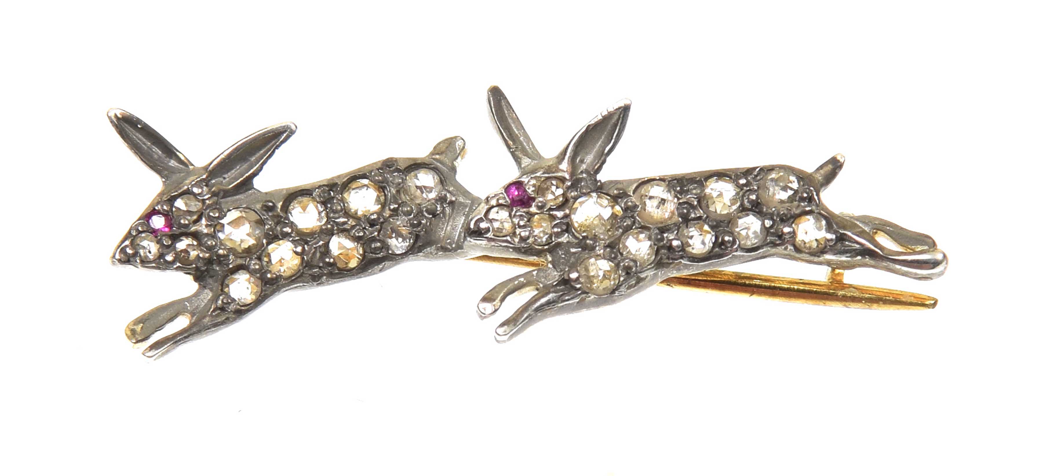 A diamond and ruby brooch Designed as a pair of rose cut diamond running rabbits, with circular