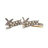 A diamond and ruby brooch Designed as a pair of rose cut diamond running rabbits, with circular