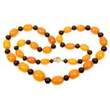 An amber and black bead necklace The graduated oval shaped amber and spherical black plastic bead