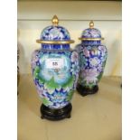 A pair of modern Oriental covered cloisonne vases decorated with flowers raised on stained wooden