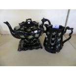 A Jackfield teapot with accompanying stand and matching jug decorated with foliate detail on a black