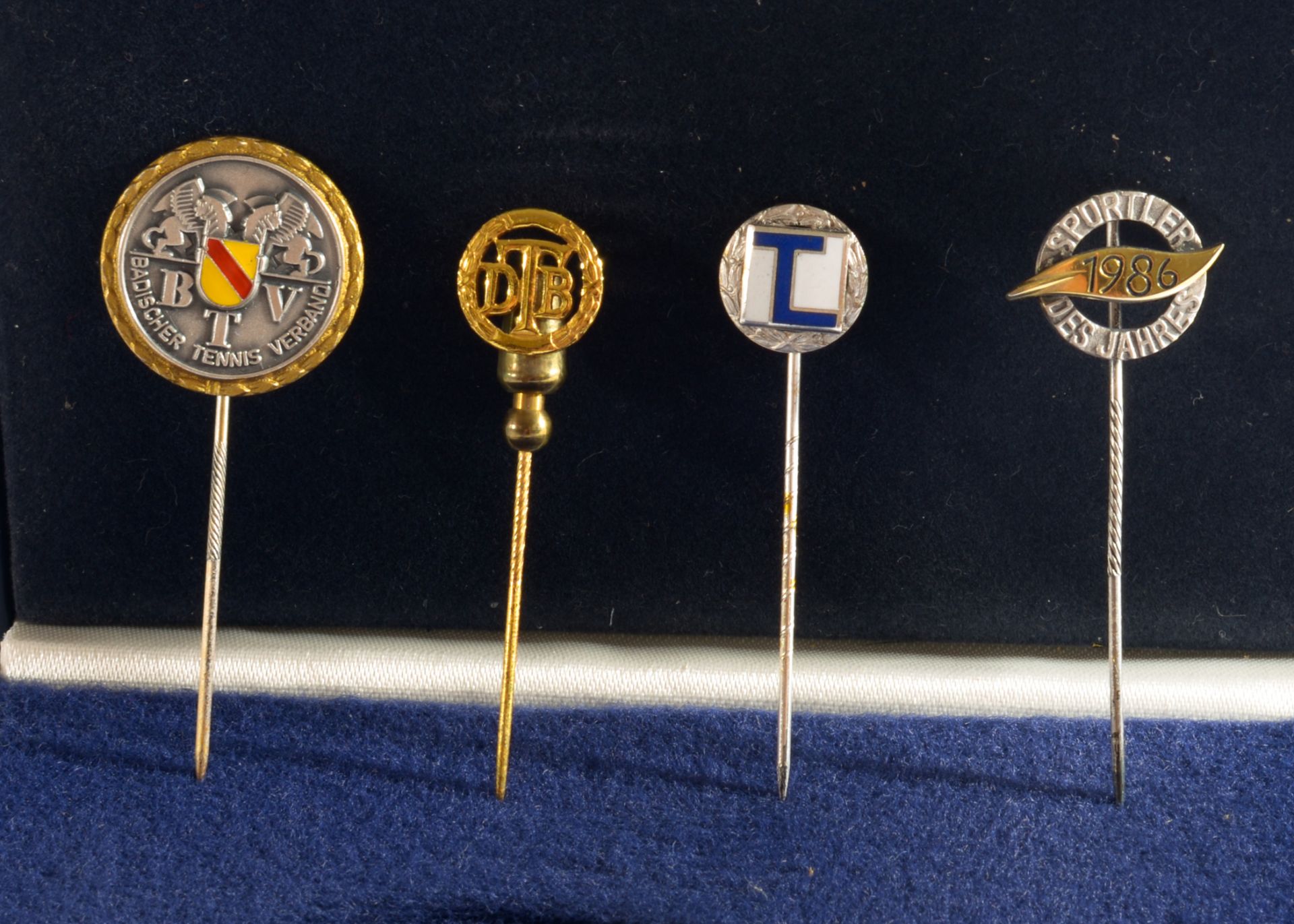 A Protective Case containing Four Lapel Pins, One bearing the words “Badischer Tennis Verband” (