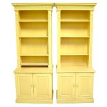 A pair of large reproduction yellow painted bookcases with moulded dentil cornice above adjustable