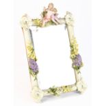 A circa 1900 Continental porcelain mirror, surmounted with two cherubic figures and decorated with