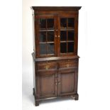 A reproduction oak bookcase on cupboard with dentil carved frieze above twin glazed doors