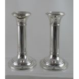 A pair of George V hallmarked silver candle sticks of plain form, raised on stepped bases,