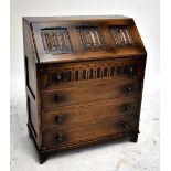A reproduction oak bureau, the fall-front with carved detail enclosing fitted interior above twin