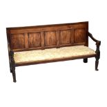 A 19th century oak settle with panelled back raised on tapering column supports, width 189cm.