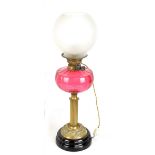 A Victorian brass oil lamp with cranberry glass reservoir and frosted shade, height 60cm (