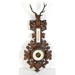 A c1900 stained beech Black Forest thermometer/barometer with stag's head above leaf carved frame,