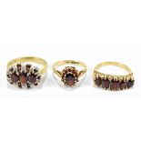 Three 9ct yellow gold dress rings all set with red coloured stones, one featuring white stone chips,