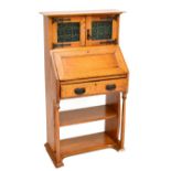 An Arts & Crafts oak bureau bookcase of small proportions, the twin cupboard doors with green and