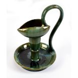 An art pottery chamber stick in the style of Linthorpe with high loop handle and green glazed